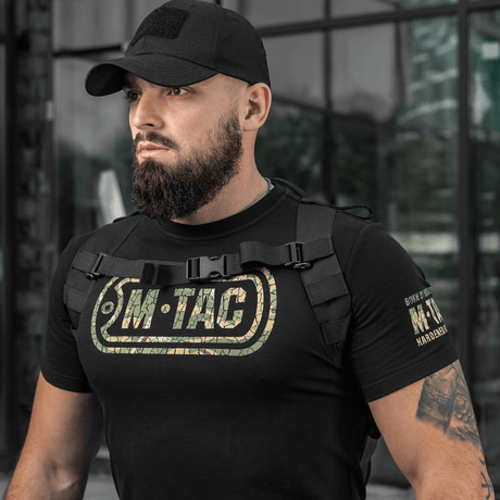Mann bærer M-Tac STURM Elite ryggsekk med svart klær, klar for taktiske oppgaver. Holdbar og allsidig for korte felteventyr.
