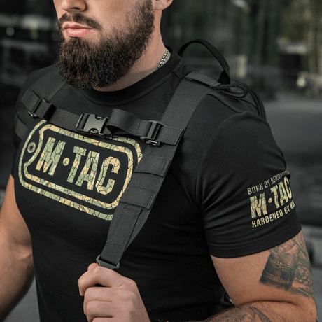 Mann iført M-Tac STURM Elite ryggsekk med taktiske stropper og M-Tac-logo på t-skjorte, ideell for korte turer.