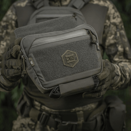 M-Tac Large Elite Gen.II skulderveske i Cordura 500D med YKK-lynlåser, sett i taktisk kamuflasjeutstyr.