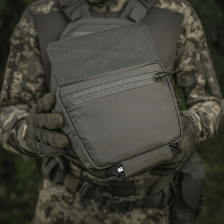 M-Tac Large Elite Gen.II skulderveske holdt av person i kamuflasje, laget av slitesterk Cordura 500D med YKK-lynlåser.
