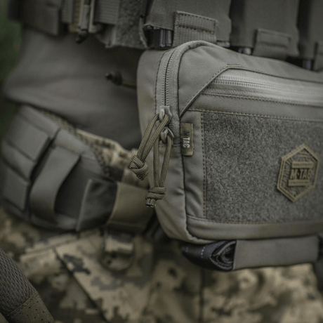 M-Tac Large Elite Gen.II skulderveske i Cordura 500D med YKK-lynlåser, ideell for taktisk bruk, sett mot kamuflasjebakgrunn.