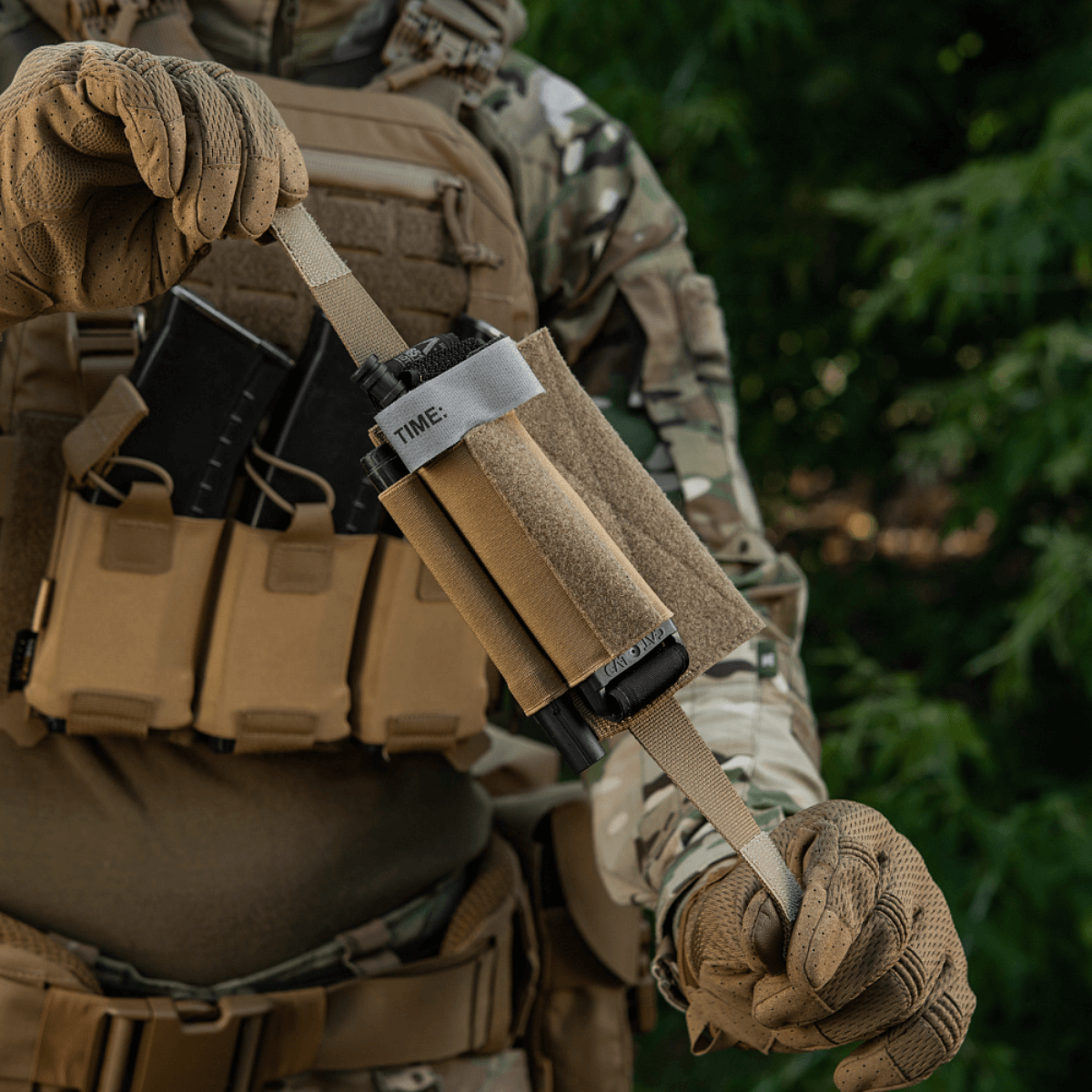 Person with tactical gear holding M‑Tac Tourniquet Pouch Elastic Gen.5 on a vest, showcasing practical use in field conditions.