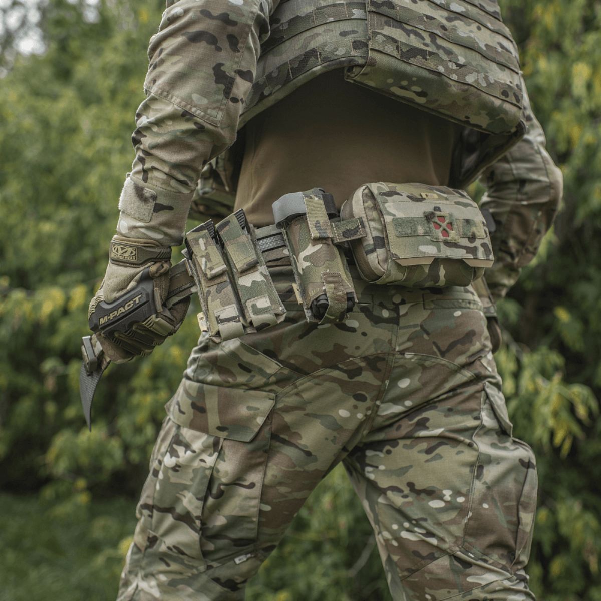Soldat med M-Tac Tiger Bælte Cobra Buckle og taktisk udstyr, set bagfra i camouflagetøj i skovmiljø.