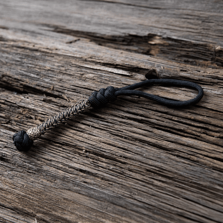 M-Tac Knife Lanyard Scandinavian i flettet paracord, et stilfullt og praktisk tilbehør til lommekniver på trebakgrunn.