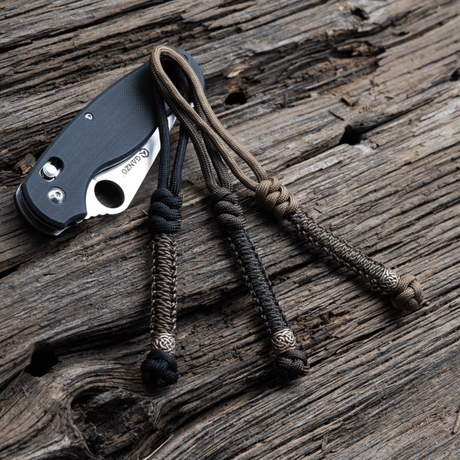 M-Tac Knife Lanyard Scandinavian stilfullt flettet paracord til lommekniver på treflate.
