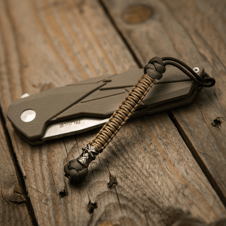 M-Tac Knife Lanyard Ninja i paracord ved siden av foldekniv på trebord