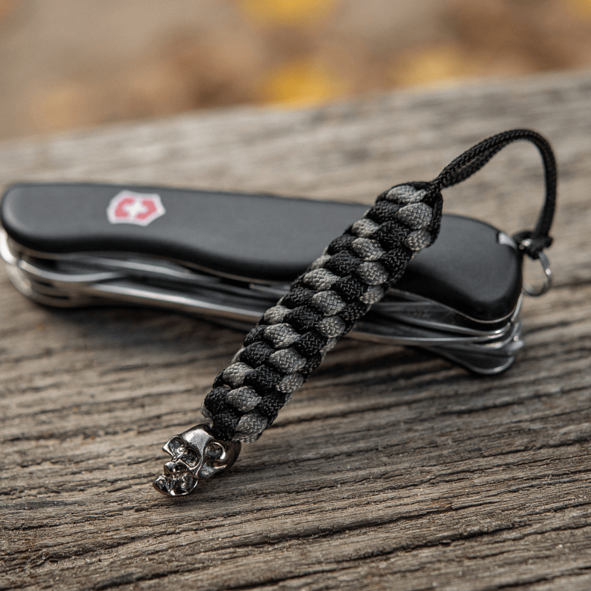 M-Tac Knife Lanyard Helix Skull ved siden af en lommekniv på træbordet, flettet paracord med kranie-design