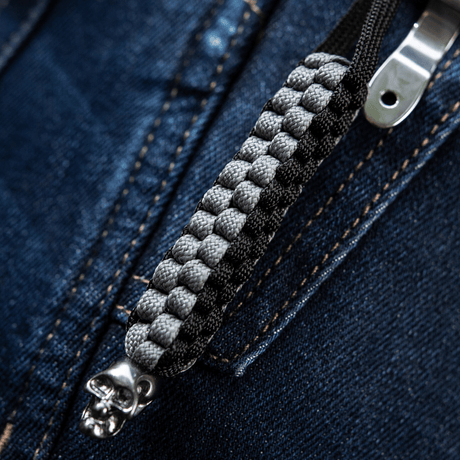M-Tac Knife Lanyard Cuboid Skull med paracord og dekorativ kranieperle på glidelåsbakgrunn, stilfullt og praktisk tilbehør.