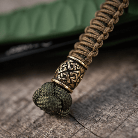 M-Tac Knife Lanyard Celtic i flettet paracord med keltisk mønster, knivtilbehør på trelignende overflate.