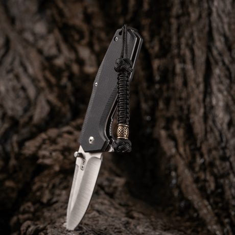 M-Tac Knife Lanyard Celtic i flettet paracord montert på en kniv mot en rustikk bakgrunn.