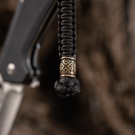M-Tac Knife Lanyard Celtic i flettet paracord med dekorativt mønster, vist på en kniv som et stilfullt og praktisk tilbehør.