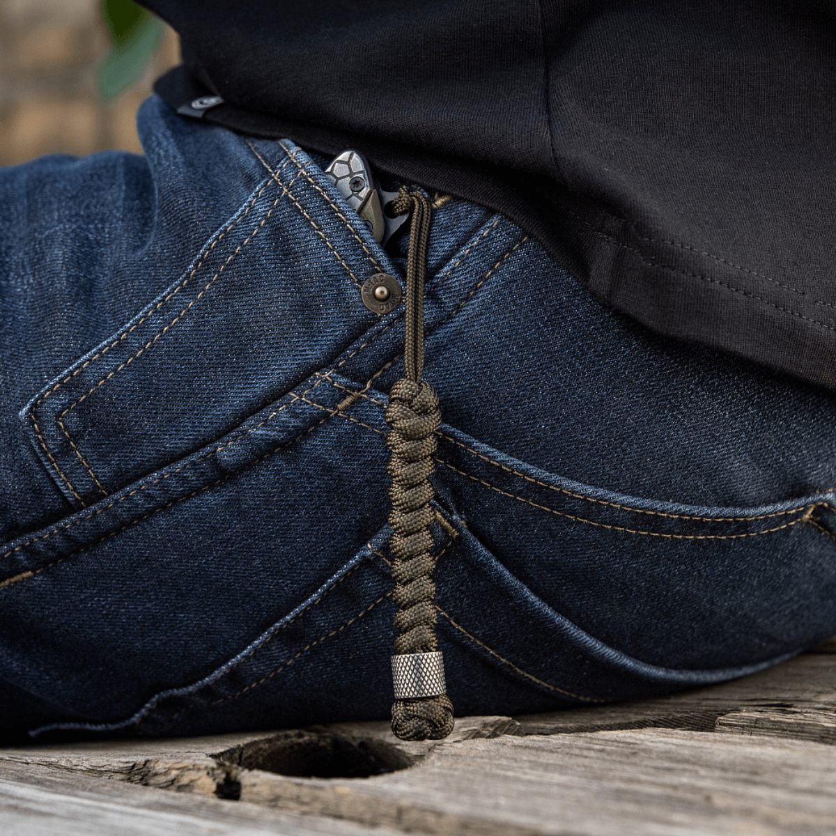 M-Tac Viper Lanyard Stainless Steel i lommen på jeans, flettet paracord med Viper-perle, fleksibel forlængelse til knivhåndtaget.