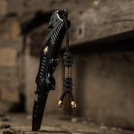 M-Tac Zeus Lanyard i flettet paracord knyttet til svart kniv på rustikk overflate, fleksibelt tilbehør for rask tilgang til utstyr.