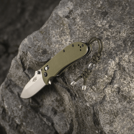M-Tac Zeus Stainless Steel Lanyard med flettet paracord og dekorativ perle for rask tilgang til kniv på steinbakgrunn.
