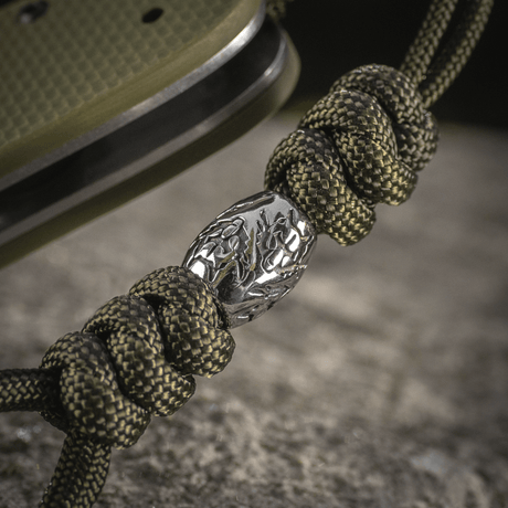 M-Tac Zeus Stainless Steel Lanyard med flettet paracord og dekorativ metallperle på en kniv, perfekt for rask tilgang.
