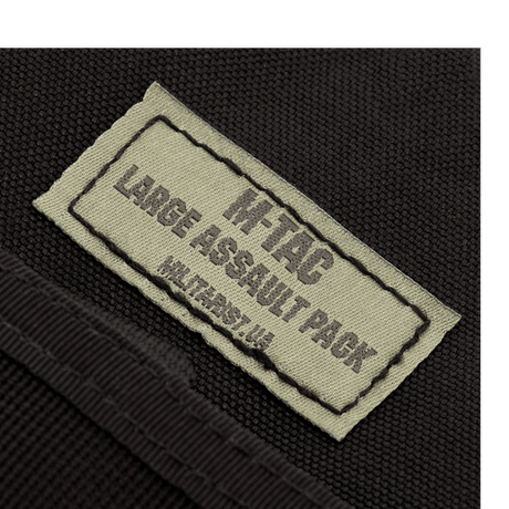 Nærbilde av etiketten på M-Tac Large Assault Pack ryggsekk som viser produktlogo og navn.