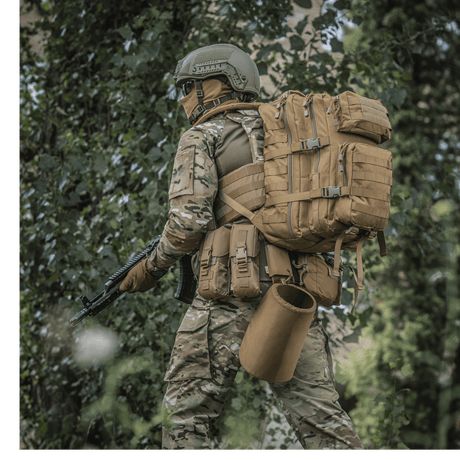 M-Tac Large Assault Pack ryggsekk i bruk av en person i kamuflasjetøy i skogmiljø, med MOLLE-system og justerbare skulderremmer.