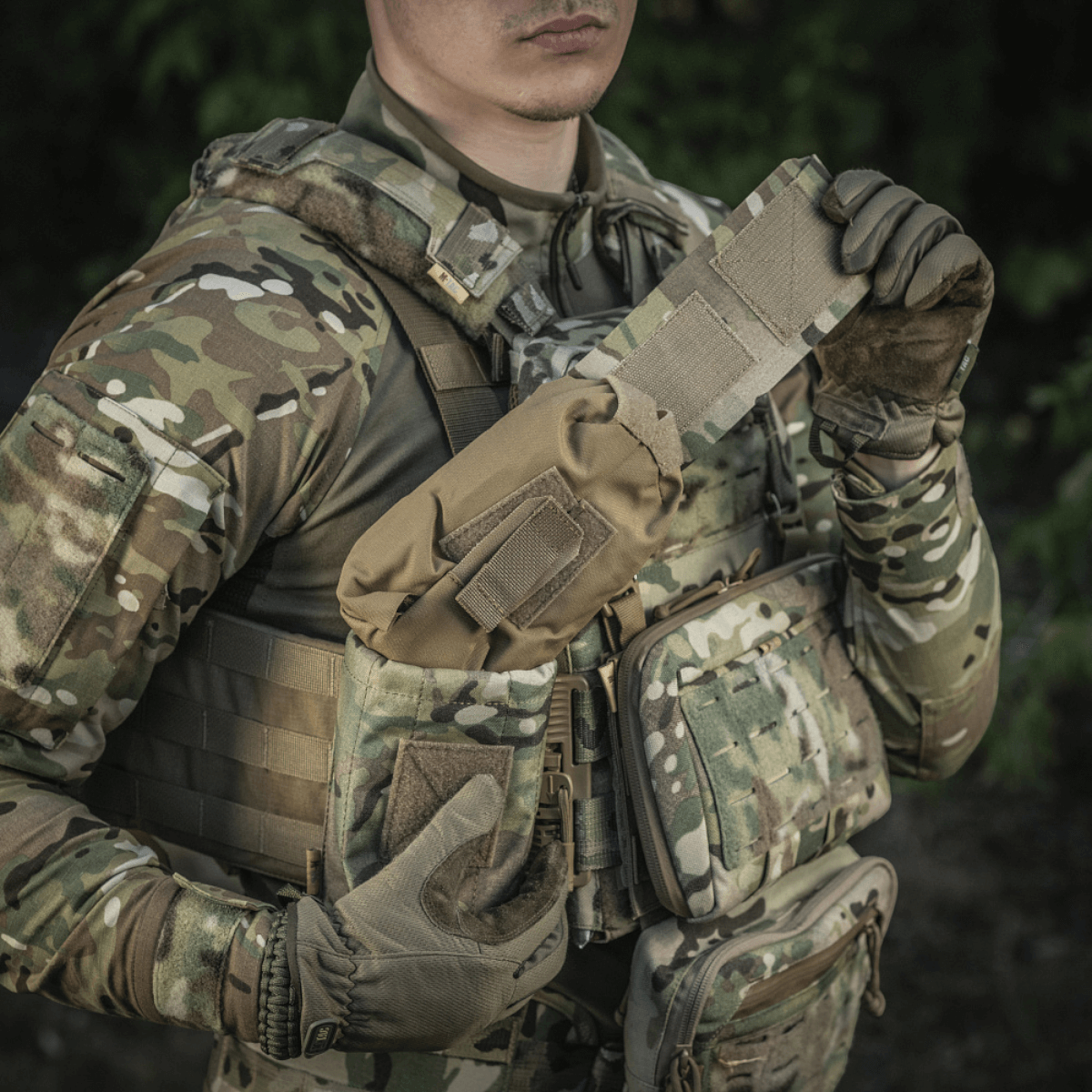 Soldat iført camouflageuniform viser M-Tac Mediclomme Small Vertical Elite i brug med IFAK-kit, lavet af slidstærkt Cordura 500D.