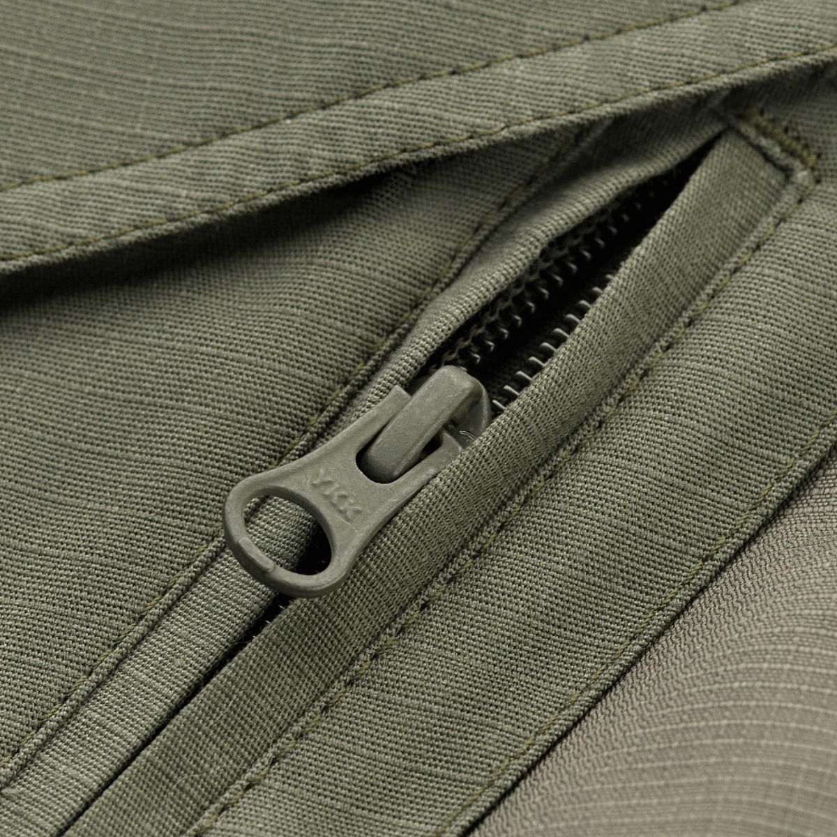 Detaljeret billede af lynlås på M-Tac Shorts Aggressor Gen.II Flex, holdbart rip-stop materiale med Teflon-belægning.