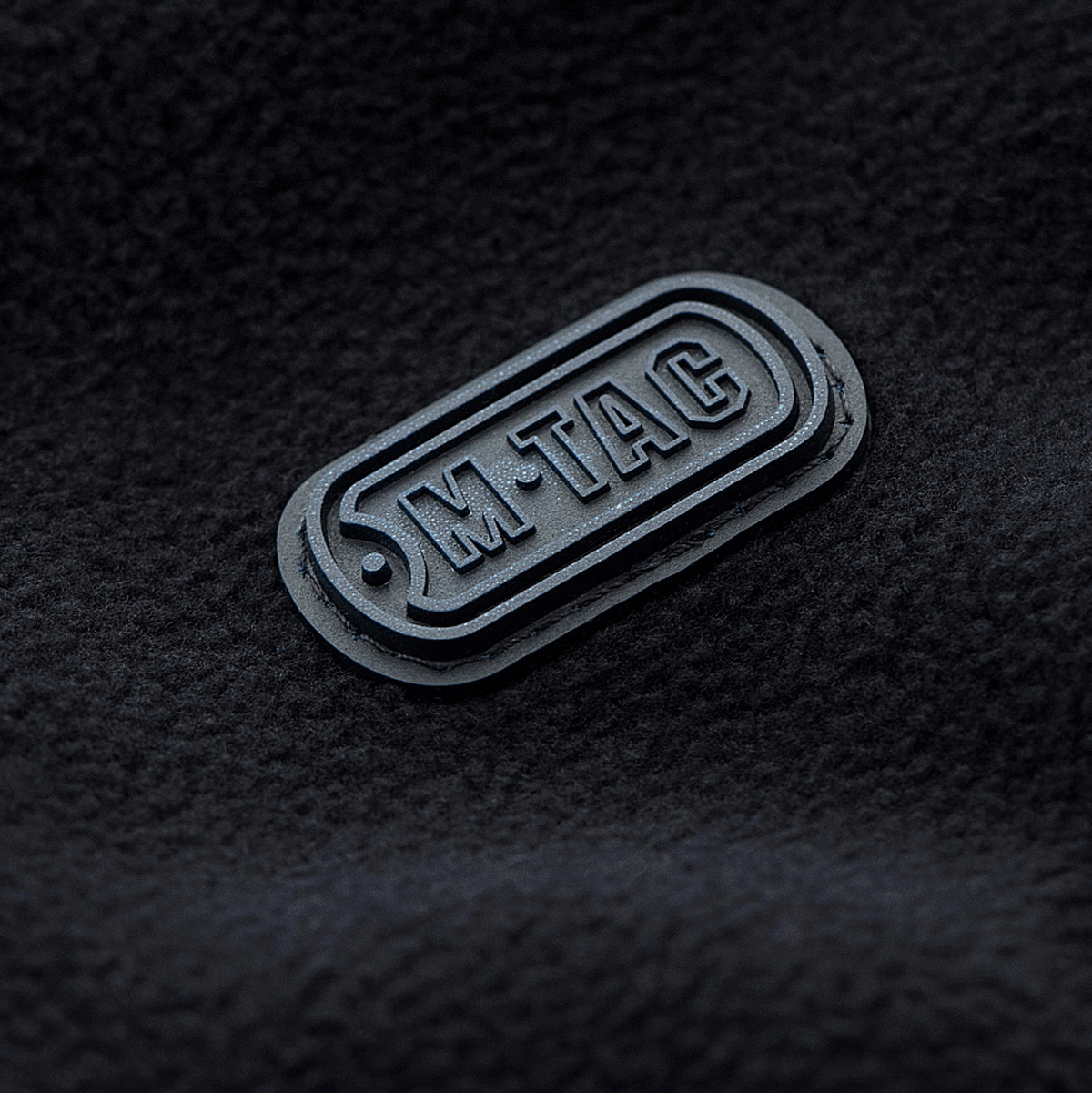 M-Tac Lite Microfleece Hættetrøje label på sort mikrofleece stof med brandlogo, fremhæver kvalitet og stil.