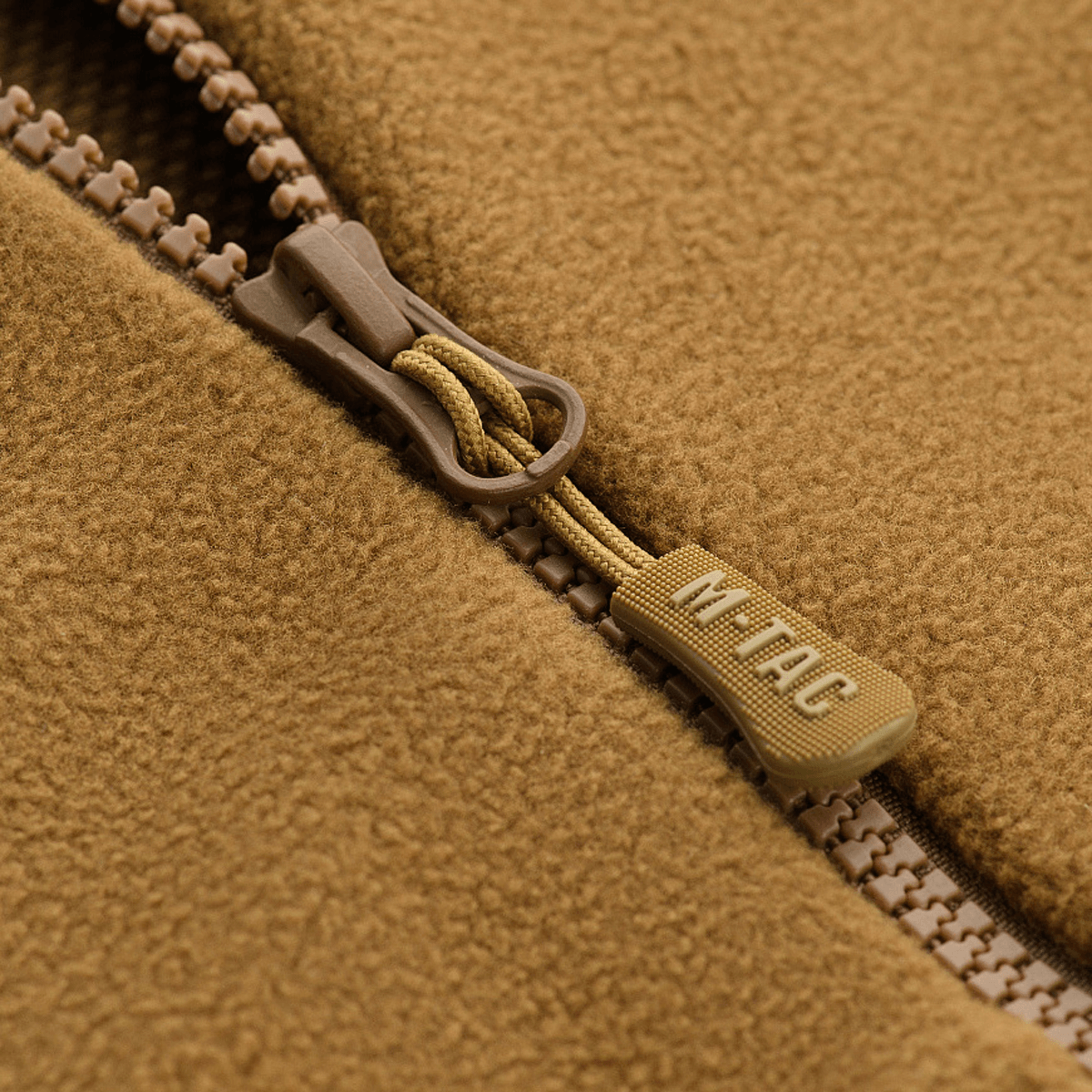 Nærbillede af lynlåsdetalje på M-Tac Lite Microfleece Hættetrøje i brun farve, der viser det elastiske mikrofleece materiale og M-Tac logo.