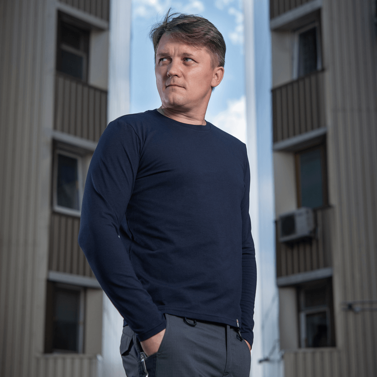 M-Tac Long-sleeve T-shirt 93/7 bæres af mand foran bygning, lavet af 93% bomuld og 7% elastan for holdbarhed og formbevaring.
