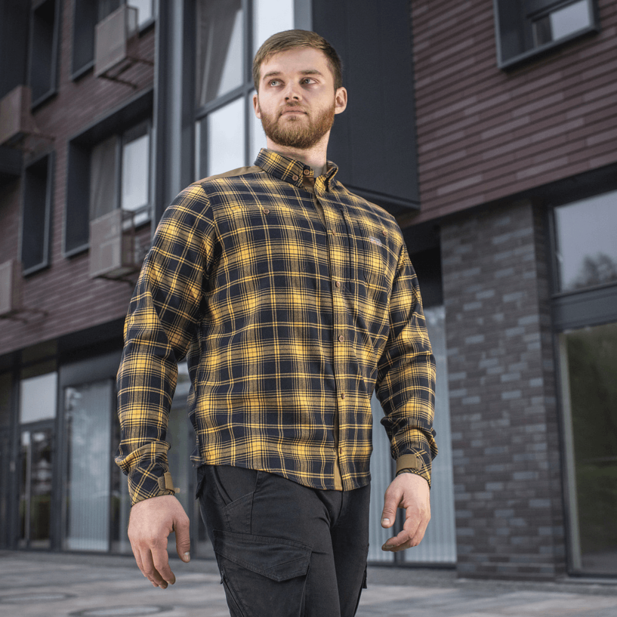 M-Tac Redneck Skjorte i navy blue/gul plaid, stilfuld og holdbar taktisk skjorte til arbejde og fritid, set på en person foran bygninger.