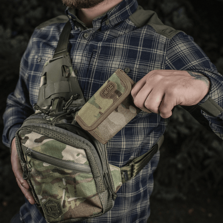 Mann holder M-Tac Pung Elite Gen.II i Cordura 500D ved siden av kamuflasjerygsekk, utendørs miljø.