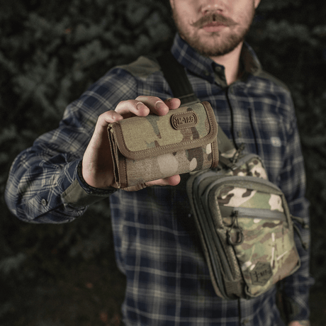 Mann holder M-Tac Pung Elite Gen.II i kamuflasje, laget av slitesterkt Cordura 500D med praktiske rom og YKK-lynlåser.