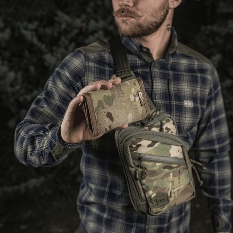 Mann holder M-Tac Pung Elite Gen.II i kamuflasjemønster, laget av Cordura 500D med YKK-lynlåser, i skogsmiljø.