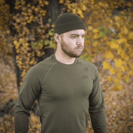 Mann iført M-Tac Raglan Athlete sweatshirt i oliven i høstlandskap, fremhever raglanermenes fleksibilitet og minimalistiske design.