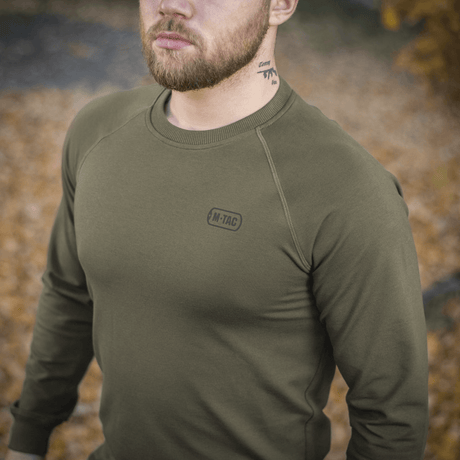 M-Tac Raglan Athlete i olivengrønn med raglanerm, perfekt for hverdag og sport, vist utendørs blant høstløv.