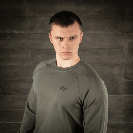 Mann i M-Tac Raglan Athlete sweatshirt i olivenfarge, viser allsidighet og minimalistisk design med raglanerm for bevegelsesfrihet.