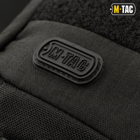 Nærbilde av M-Tac-logoet på M-Tac Buckler Taske Elite, en svart taktisk veske med MOLLE-system og skjult våpenrom.