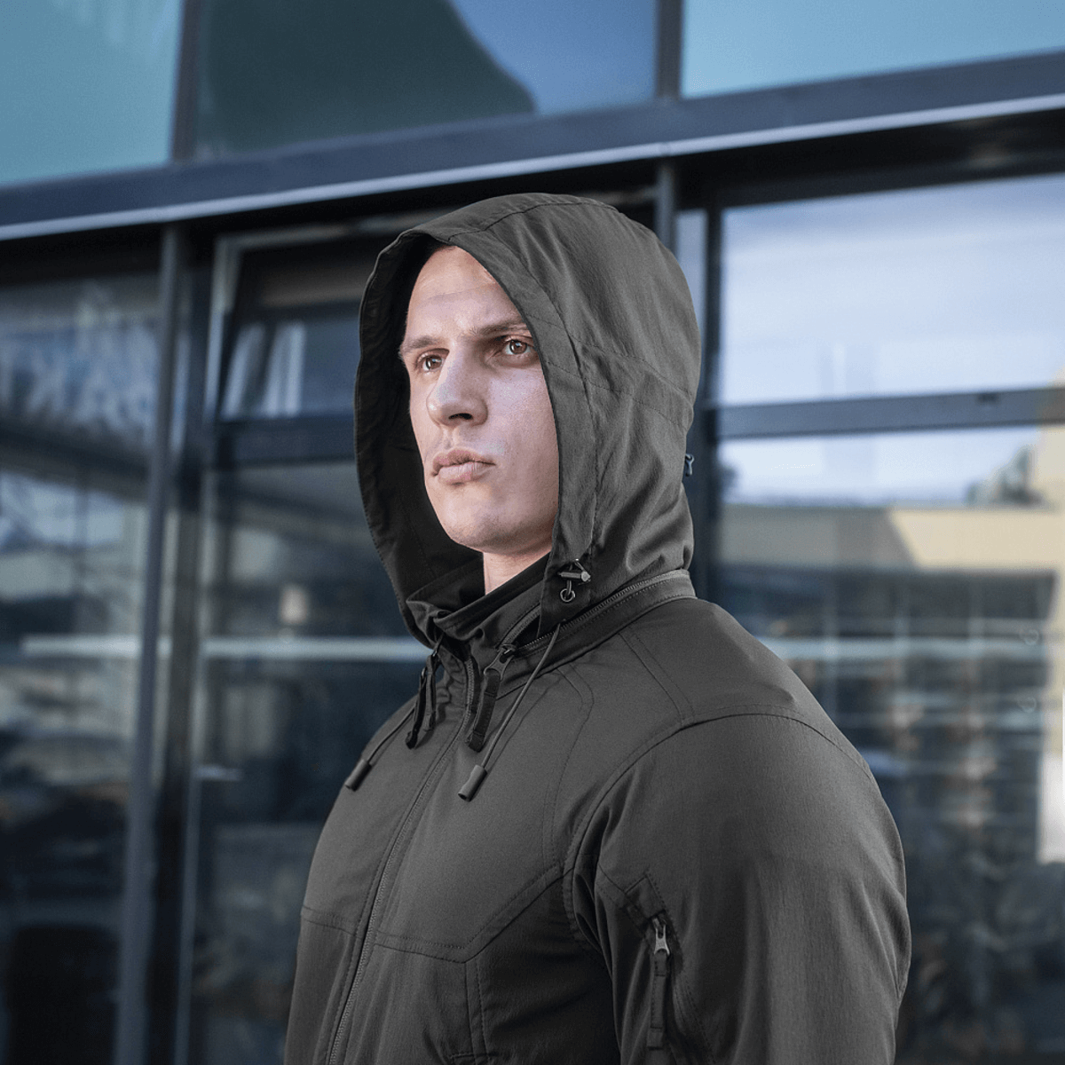 M-Tac Flash Jakke i minimalistisk design, velegnet til udendørs aktiviteter som vandreture og sport, set på en person foran en bygning.