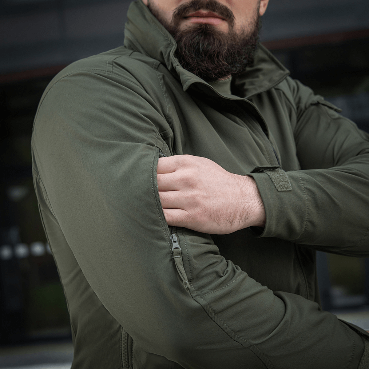 Mand bærer grøn M-Tac Flash Jakke, letvægts og alsidig til udendørs aktiviteter, ses justere jakken uden velcrofelter.