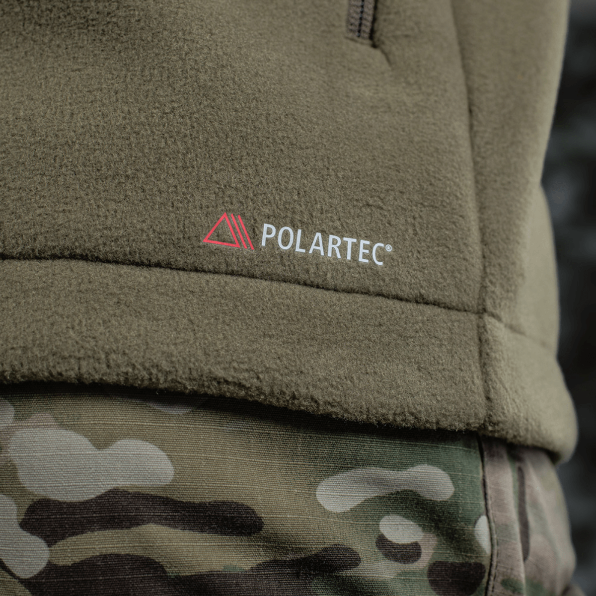 M-Tac Combat Fleece Polartec Jakke med Polartec logo og camouflagebukser, perfekt til taktisk brug, viser detaljer af materialet.