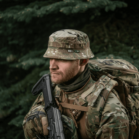 Mand iført M-Tac Panama Hat Gen.II NYCO i camouflagedesign, ideel til outdoor-brug og militærstil, med rygsæk i skovmiljø.