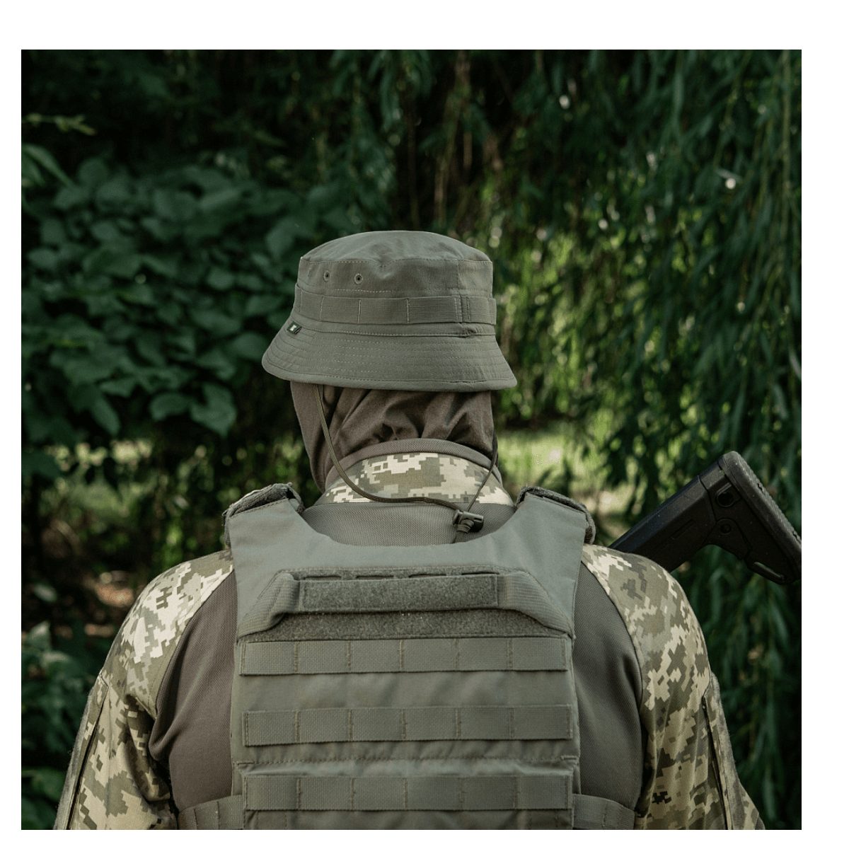 Person i camouflageuniform med hjelm og vest i skov.