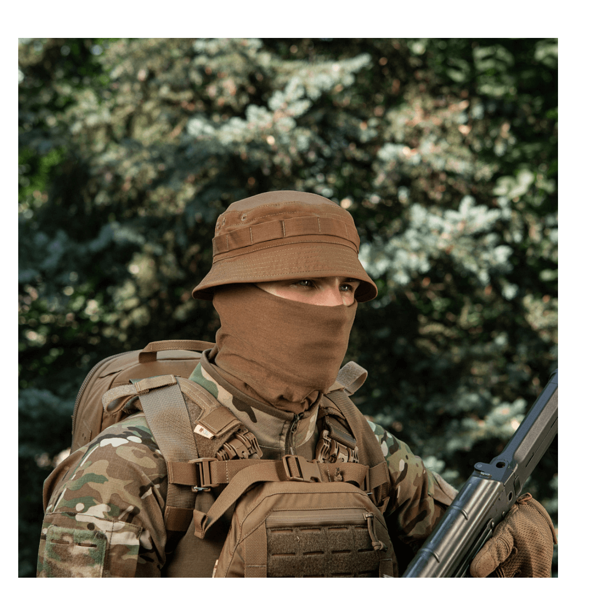 Person iført M-Tac Panamahat Gen. II Flex Rip-Stop i skovområde, bærende camouflage outfit og udendørsudstyr.