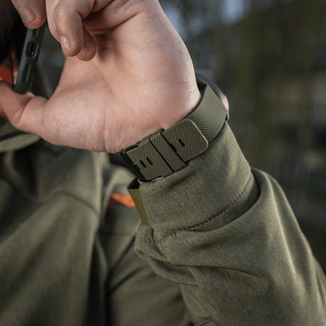 Person som bruker M‑Tac multifunksjonelt taktisk ur med robust urkasse og rem, ideelt for friluftsliv og militærbruk