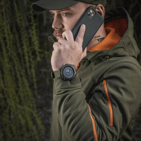 Mann iført M‑Tac multifunksjonelt taktisk ur mens han snakker i telefon, skogbakgrunn