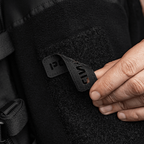 Person fester M‑Tac Patch Poland End-to-End 25x80 til klær med velcro, viser detalj av laserskåret inskripsjon og holdbart Cordura 500D-materiale.