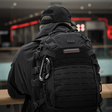 En person med ryggsekk iført M-Tac Patch Flag 25x80 Mini Squares i Cordura 500D med velcrofeste, passende for taktisk utstyr.