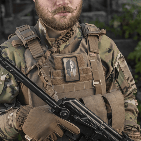 M-Tac Spartan Hjelm Patch i bruk på taktisk vest, symboliserer mot og styrke, vintage Spartan-design, velcro-festing til utstyr.