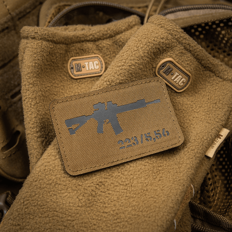 M-Tac AR-15 223/5,56 Laser Cut-patch festet på brunt taktisk teppe med M-Tac-logoer, designet for utendørs og militær bruk.