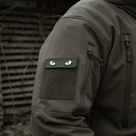 M-Tac Cat Eyes 3D PVC-patch på jakkeermet i et taktisk miljø, viser lysreflekterende og fluorescerende design, festet med Velcro.