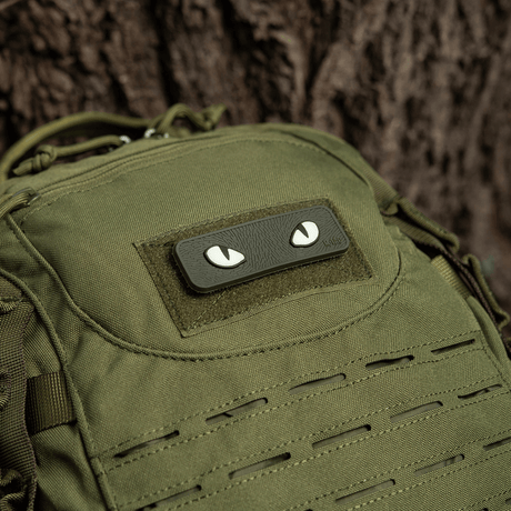 M-Tac Cat Eyes 3D PVC-patch på grønn ryggsekk ved siden av et tre.