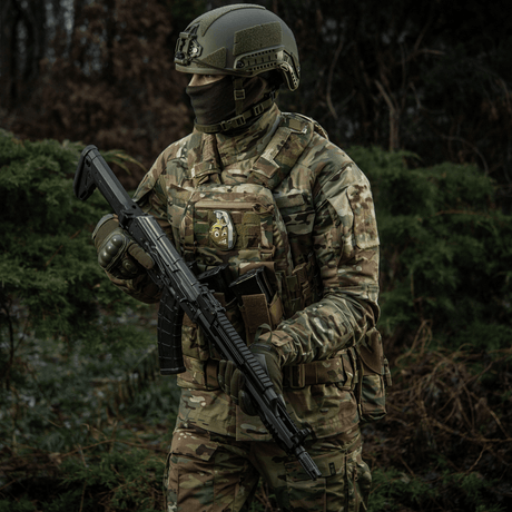 En soldat i kamuflasje med M-Tac Patch M67 Granat 3D PVC på vesten, iført taktisk utstyr i skogmiljø.