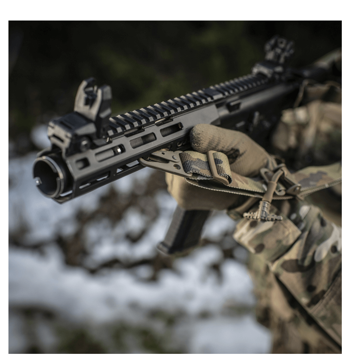 Jægers hånd med M-Tac Universal Våbenrem på et gevær i sneklædt terræn for maksimal komfort og fleksibilitet i våbenhåndtering.